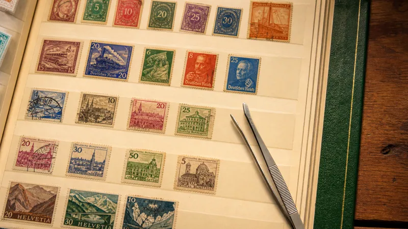 Open stamp album page with rows of vintage postage stamps and philatelic tongs resting on the page